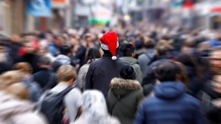 Mitten in einer hektischen Menschenmenge steht eine einzelne Person mit Weihnachtsmütze.