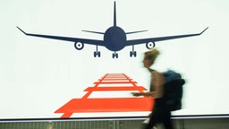 Eine Frau geht auf dem Frankfurter Flughafen am Rande des Fernbahnhofes an einer Werbetafel vorbei, die für das kombinierte Reisen mit Bahn und Flugzeug wirbt. 