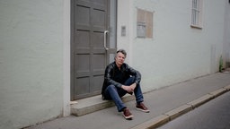 Jurist und Autor Thomas Galli sitzt vor einem Hauseingang. 