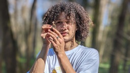 Tristan Jurisch steht im Wald und begutachtet einen Pilz. 