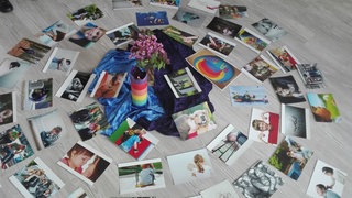 Um eine Bumenvase auf dem Boden liegen Fotos, Postkarten und Bilder