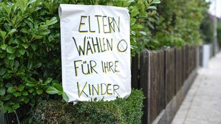 Ein handgeamltes Plakat an einer Hecke mit der Aufschrift "Eltern wählen für ihre Kinder"