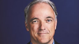 Porträtaufnahme von Werner Bartens: Er ist glattrasiert, trägt kurzes graues Haar und hat blaue Augen.