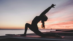 Eine Frau übt Yoga im Sonnenuntergang am Strand aus