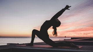 Eine Frau übt Yoga im Sonnenuntergang am Strand aus