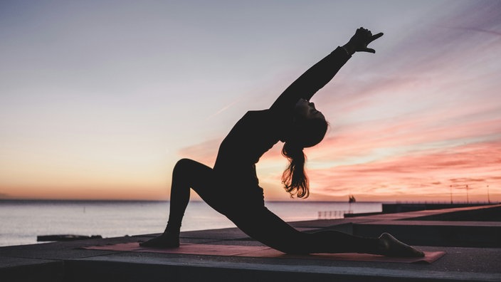 Eine Frau übt Yoga im Sonnenuntergang am Strand aus