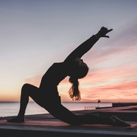 Eine Frau übt Yoga im Sonnenuntergang am Strand aus