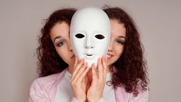 Junge Frau mit einer Maske vor dem Gesicht, trauriges und fröhliches Gesicht
