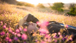 Frau liegt im Sonnenuntergang auf einer Blumenwiese