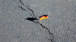 Ein Deutschlandfaehnchen steckt in einem Asphaltriss und symbolisiert den Riss in der deutschen Gesellschaft.