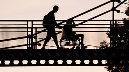 Rollstuhlfahrer wird im Sonnenuntergang über Brücke geschoben