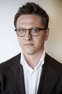 Hanno Sauer mit Brille und im Anzug vor einem neutralen Hintergrund