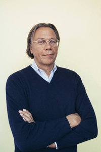 Ein Mann mit Brille und im dunkelblauen Pullover vor einem neutralen Hintergrund.