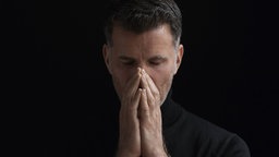 Ein verzweifelter Mann, der unter geschlossenen Augen das Gesicht in den Händen vergräbt