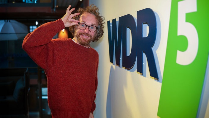 Friedemann Weise steht lachend vor dem WDR-5-Logo