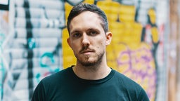 Portraitfoto von Max Osswald vor einer Mauer mit Graffiti, Foto: Pierre Jarawan