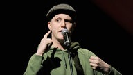Sebastian23 alias Sebastian Rabsahl steht bei einer Veranstaltung auf einer Bühne.