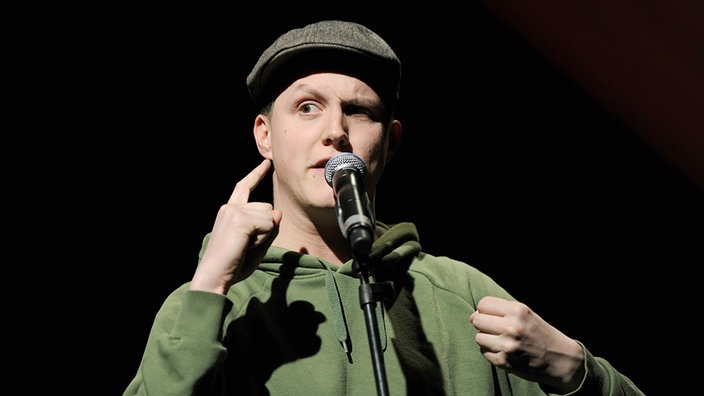 Sebastian23 alias Sebastian Rabsahl steht bei einer Veranstaltung auf einer Bühne.