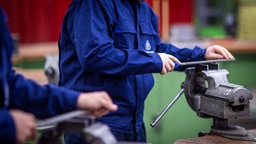 Lehrlinge arbeiten mit einer Metallfeile an Schraubstöcken in einer Lehrwerkstatt