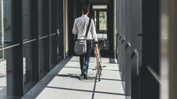 Ein Angestellter eines Unternehmens schiebt sein Fahrrad durch einen Büroflur. 
