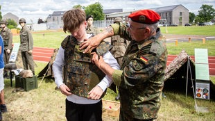 Ein Bundeswehrsoldat zieht einem Jugendlichen eine Bundeswehr-Weste an beim Bundeswehr-Tag für Besucher in Unna am 06.06.2026