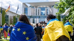 Zwei Demonstrierende mit EU- und Ukraine-Glagge stehen vor dem Bundeskanzleramt in Berlin