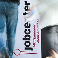  Personen gehen am Logo vom Jobcenter vorbei.