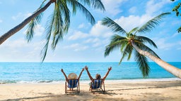 Glückliches Paar mit erhobenen Armen entspannen am Strand und genießen das Meer auf einer tropischen Insel. 