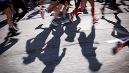 Nauaufnahme der Beine und Schatten Marathonlaufender auf einer Straße.