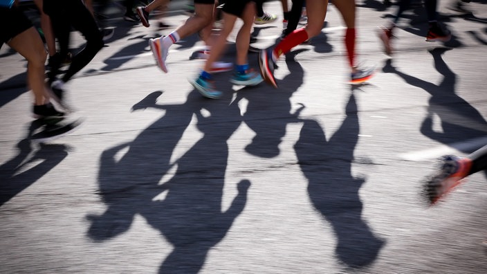 Nauaufnahme der Beine und Schatten Marathonlaufender auf einer Straße.