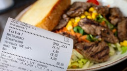 Eine Rechnung mit Mehrwertsteuer neben einem vollen Teller in einem Restaurant.