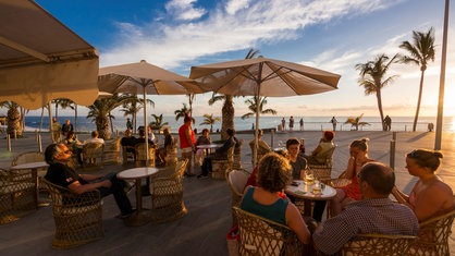 Touristen essen unter Palmen an der Strandpromenade eines spanischen Strands.