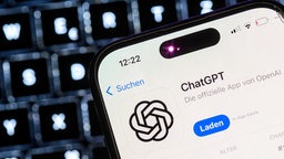 Smartphone mit der App des KI-Chatbots ChatGPT ist vor dem Logo des US-Softwareunternehmens OpenAI zu sehen.