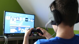Eine Person hält einen PS4 Controller in seinen Händen und spielt ein Computerspiel am Fernseher.