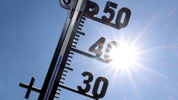 Die Sonne strahlt vom blauen wolkenlosen Himmel, im Vordergrund ist ein Thermometer zu sehen.