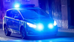 Polizeieauto fährt mit Blaulicht am Abend durch eine Straße. 