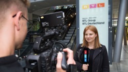 Journalistin wird während eines Interviews vor dem Firmenschild "RTL Group" fotografiert. 