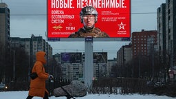 Frau schiebt einen Kinderwagen an einer Werbetafel vorbei, Petersburg, Russland, 21.01.2026.