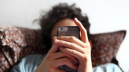Junger Mann blickt auf ein Smartphone. 