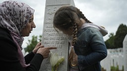 Mädchen auf dem Potocari-Gedenkfriedhof in Srebrenica, Bosnien und Herzegowina,  umarmt den Grabstein ihres Großvaters, den sie nie kennengelernt hat, 10.07.2025.