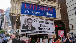 Menschen halten zur Unterstützung des Moderators Stephen Colbert ein Protest-Schild gegen die Absetzung der Late Show mit der Aufschrift: Colbert Stays! Trump Must Go!, Ed Sullivan Theater, New York, 21.07.2025.