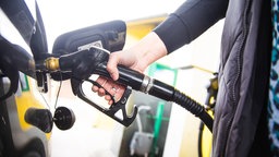 Frauenhände halten eine Zapfpistole beim Tanken eines Fahrzeugs an einer Tankstelle.