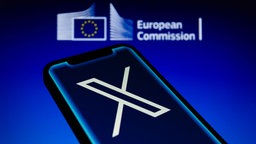 Logo der Europäischen Kommission wird hinter dem X-Logo auf einem Smartphone angezeigt. 