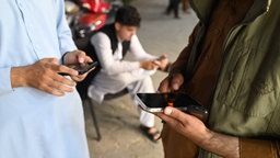Drei afghanische Männder schauen auf ihre Smartphones nachdem die Taliban 48 Stunden Mobilfunk und Internet lahmgelegt hatten.
