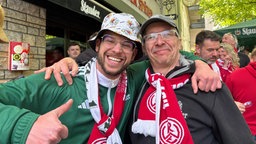 Zwei Männer umarmen sich nach dem Apfiff und lachen in die Kamera.