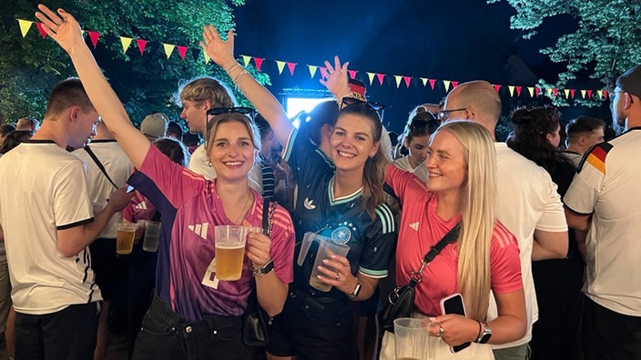 Drei junge Frauen freuen sich in Fußballtrikots