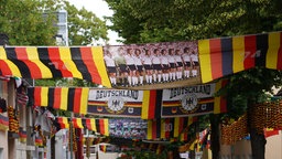 Dutzende Deutschlandflaggen und Mannschaftsfotos hängen über einer Straße.