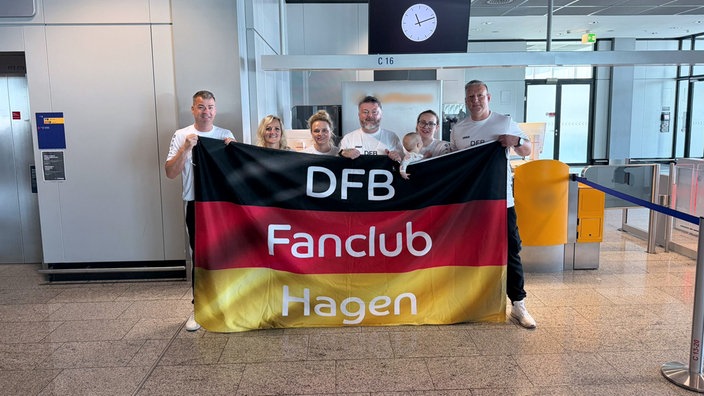 Sechs Personen halten eine große Deutschlandflagge mit der Aufschrift "DFB Fanclub Hagen" vor sich.