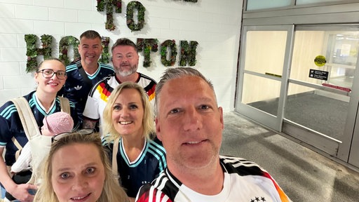 Die Hagener machen bei ihrer Ankunft in Houston ein Selfie und tragen Fußballtrikots, im Hintergrund steht "To Houston" an der Wand.