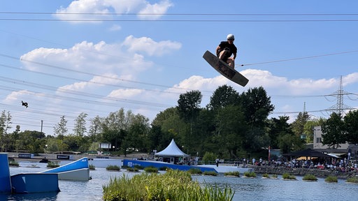 Ein Wakeboarder fliegt mit seinem Board durch die Luft über einem See